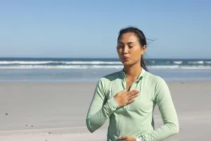 Relaxed Prints: Mid-adult Asian woman practicing breathing at sandy beach in light green zip-up top