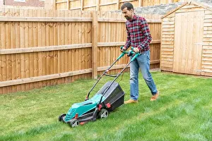 Checked Prints: Mid adult man cutting grass with lawn mower at backyard