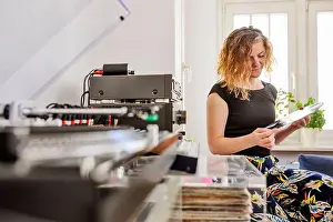 Mid Adults Prints: Mid adult woman holding record while sitting by stereo system at home
