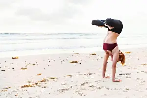 Practising Prints: Mid adult woman upside down in yoga position on beach