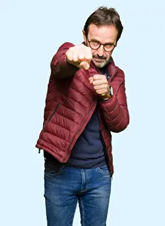 Aggressive Prints: Middle age handsome man wearing glasses and winter coat Punching fist to fight