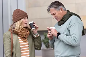 Mature Adult Prints: Middle-aged couple standing on sidewalk holding coffee cups