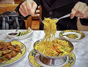 Stockimo Prints: Midsection of a man picking up vermicelli noodles with fork and spoon from serving dish on table at restaurant