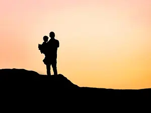 Back Lit Prints: Minimalist silhouette of a grandfather holding his grandson on a hilltop in Cape Zebib