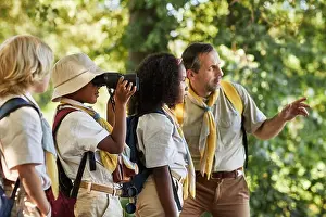 Preteen Prints: Mixed-race boy scout wearing hat and backpack using binoculars while standing near classmates
