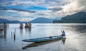 Cruelty Prints: A M'nong ethnic minority man guides his canoe to shore at dusk while Vietnamese tourists ride on three elephants