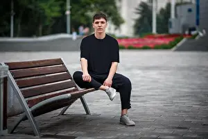 Blurred Background Prints: Mockup of a black casual t-shirt on a guy sitting on a blurred background of a park