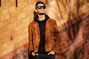 Eyewear Prints: Model looking man stand near the wall and hold his glasses towards the sun shine