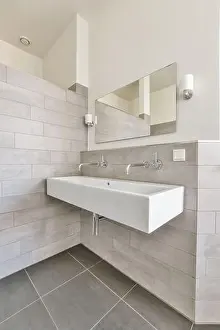 Faucet Prints: a modern bathroom with grey tiles and white fixtures on the wall above the sink is a large mirror in the corner