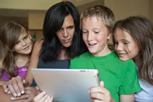 Sibling Prints: Mom and her three kids looking at an ipad together
