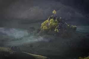 Morning sunshine with fog over a mountain landscape with a rock and trees in direct sunlight. Fundatura Ponorului, Romania