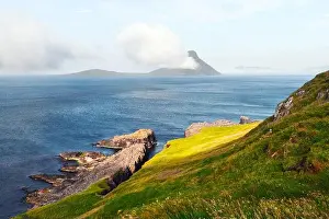 Morning view onto the Faroese island Koltur with spectacular clouds and blue water in a dramatic valley with mountain range. Faroe Islands, Denmark