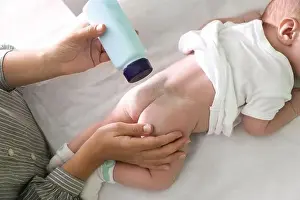 Buttocks Prints: Mother applying dusting powder at baby's buttocks on changing table, above view