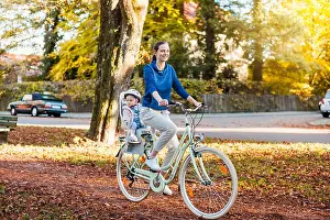 Mid Adults Prints: Mother and daughter riding bicycle, baby wearing helmet sitting in children's seat