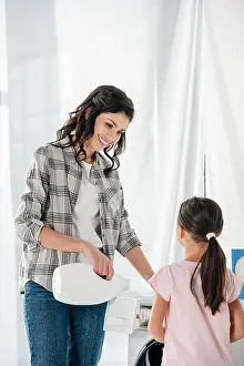 Laundry Room Prints: mother in grey shirt pouring liquid laundry detergent in washer wile daughter in pink t-shirt standing near in laundry