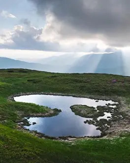 Mountain lake on sunrise time. Picturesque summer landscape with green mountain hills and sun rays in morning sky. Carpathian mountains