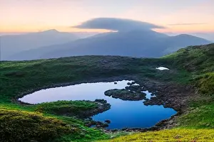 Mountain lake on sunrise time. Picturesque summer landscape with green mountain hills and sun rays in morning sky. Carpathian mountains