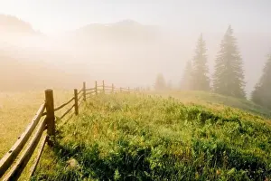 Mountain valley during sunrise. Woden fence on foggy meadow. Located place: Carpathians, Ukraine, Europe