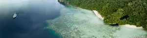The mouth of a dark, water-filled cave opens on the edge of a forest-covered limestone island near Fak Fak, Indonesia. Limestone often harbors caves