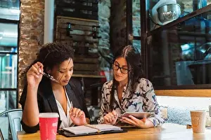 Beautiful Woman Prints: Multi-ethnic female colleagues discussing over digital tablet and diary while sitting at coffee shop during meeting
