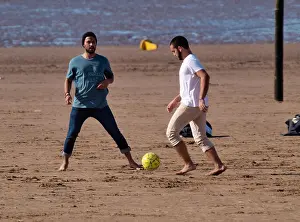 Immigrant Prints: Multi-racial group of young men playing football on the beach