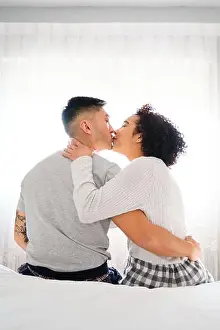 Honeymoon Prints: Multiethnic romantic couple kissing sitting in bed backlighting