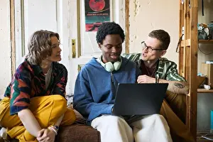 Medium Shot Prints: Multiethnic young adults collaborating on laptop while sitting together