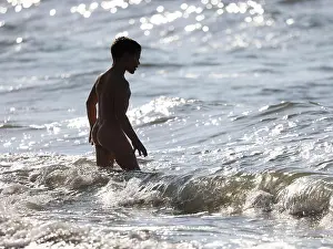 Naked young boy entering to sea, in sea waves