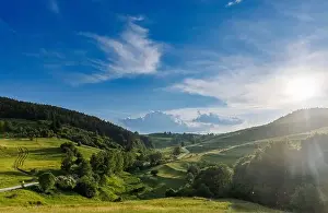 A narrow automobile paved intermountain road passes and meanders among low hills covered with spruce forests