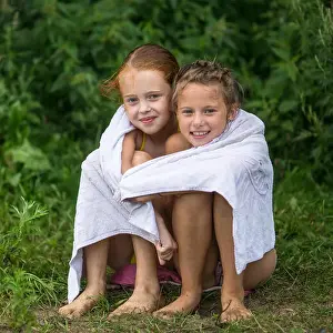 Two naughty little girls sitting on the beach in a towel after a bathe in the lake