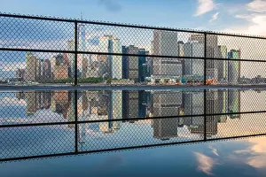 New York, New York, USA city skyline of Lower Manhattan on the New York harbor through fencing