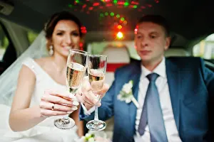 Gown Prints: Newly married couple drinking champagne in the limousine on their wedding day