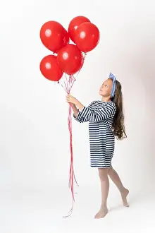 Full Shot Prints: Nosy girl holding bunch of red balloons in two hands and looking at balloons