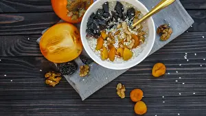Oatmeal with Persimmon, Prune, Dried Apricots, Walnut and Sesame on a Black Wooden Table Top View Copy Space Background