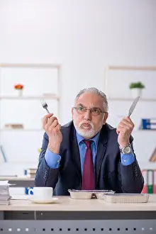Executive Prints: Old businessman employee having breakfast at workplace