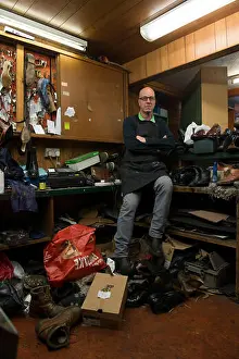 High Street Prints: an old fashioned shoe repair / cobbler fixes shoes in his busy shop using traditional techniques and tools