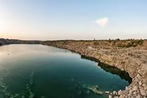 Old flooded stone quarry with large stones in the evening warm bright light covered with small dry plants in