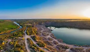 Old flooded stone quarry with large stones in the evening warm bright light covered with small dry plants in