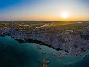 Old flooded stone quarry with large stones in the evening warm bright light covered with small dry plants in