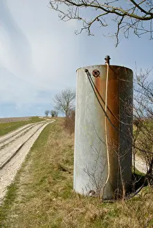Galvanized Prints: Old rivetted galvanised steel tank with hoses beside chalky farm track on the South Downs