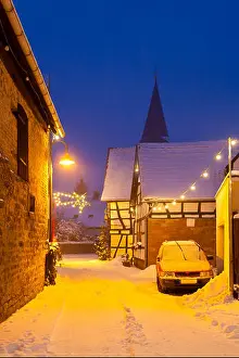 Snowfall Prints: An old street with half-timbered houses and christmas lights at night during snowfall in Lachen
