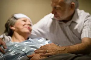 Fever Prints: Old woman in pain lying bed holding hands with husband