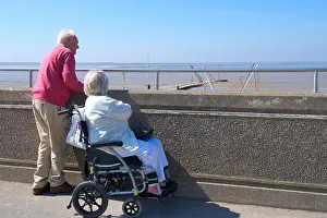 Disability Prints: Older couple looking over promenade wall to beach of Burnham-on-Sea, Somerset