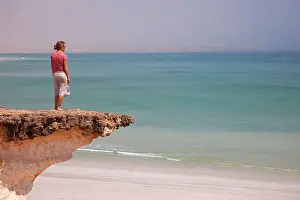 Oman Prints: Oman, Duqm. A young lady stands at the edge of a precarious cliff overlooking the Arabian Sea