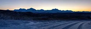 Hoof Prints: Orange sky behind mountain range after sunset on a snowy roadvnear Delta Junction, Alaska