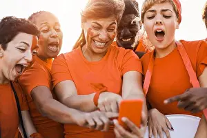 Team Sport Prints: Orange sport supporters watching football game on mobile phone - Focus on center woman face