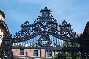 Harvard University Prints: An Ornate iron gate and the historical brick buildings of Harvard University in Cambridge