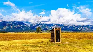 Glaciers Prints: An Outhouse at Mormon Row with in the background cloud covered Peaks of the Grand Tetons In Grand Tetons National Park