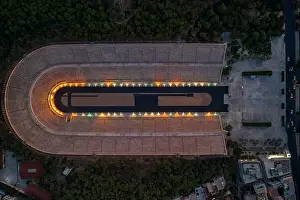 Gods View Prints: Overhead aerial drone shot of Panathenaic marble stadium with lights in dusk Pangrati