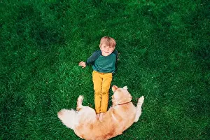 Primary Age Child Prints: Overhead view of a boy lying on grass playing with his golden retriever dog